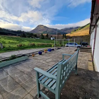 a blue bench on a patio with a view of a mountain at Sachsblick in Lochgoilhead