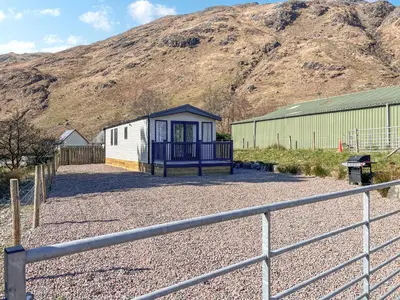 a building with a fence and a mountain in the background at Katie's Cosy Caravan - Uk48380 in Ardgour