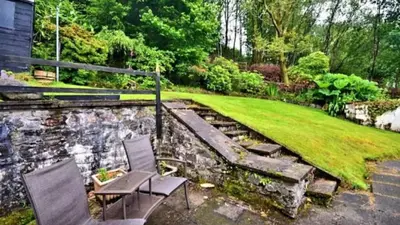 a garden with two chairs and a stone wall at Rowantree Cottage in Arrochar