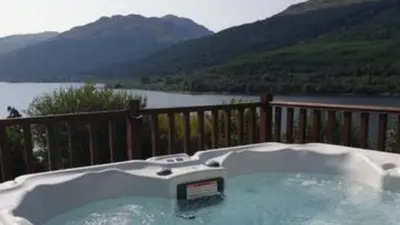 a hot tub on a deck with a view of a lake at TheLodge in Arrochar