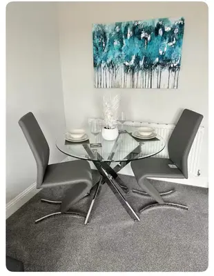 a glass table and chairs in a room with a painting at Modern staycation Apartment in Caldercruix