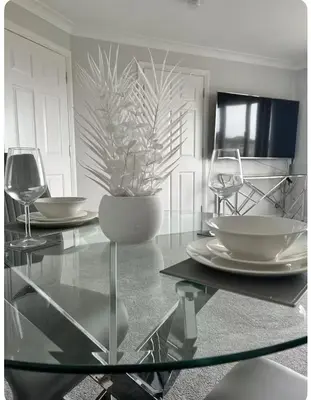 a glass table with plates and wine glasses on it at Modern staycation Apartment in Caldercruix