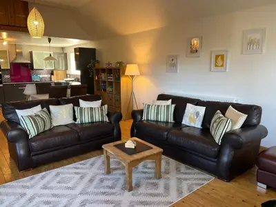 a living room with black leather couches and a table at Callanish Bothy in Benderloch