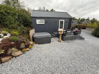 a small black shed with a bench and some plants at Tumpseys Hideaway with Hot Tub & Sunset Loch Views, Glencoe Near Fort William in Ballachulish