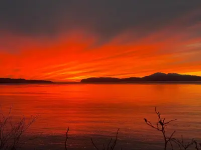 a sunset over a large body of water at Tumpseys Hideaway with Hot Tub & Sunset Loch Views, Glencoe Near Fort William in Ballachulish