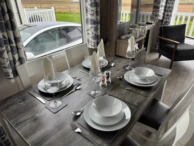 a table with plates and glasses and a car in the background at The Retreat - Turnberry Holiday Park Amazing Sea View in Girvan