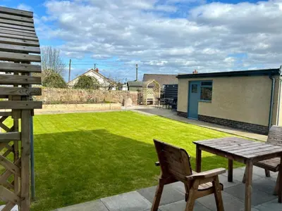 a patio with a wooden table and a lawn at Dunmuir House 4 Bedroom 2 bathroom House & Garden in Denny in Falkirk