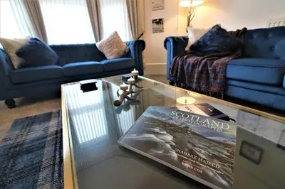 a living room with a glass table with a book on it at 10 Bedrooms Pool Table Garden Piano in Glasgow