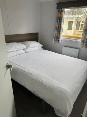 a bedroom with a bed with white sheets and a window at 131 Loch View Three Lochs Holiday Park in Newton Stewart