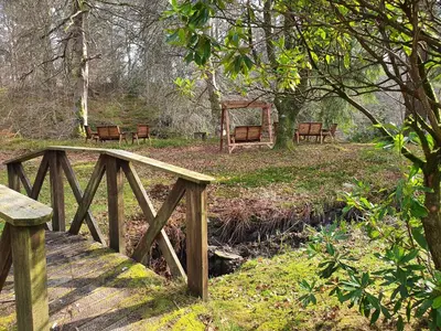 a wooden bridge with benches in a forest at The River Inn in Killin