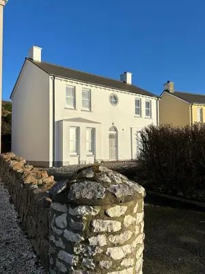 a white house with a stone wall in front of it at Church Bay House in Rathlin Island
