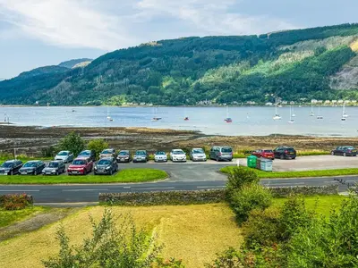 a parking lot with cars parked next to a body of water at Heatherdale in Dunoon