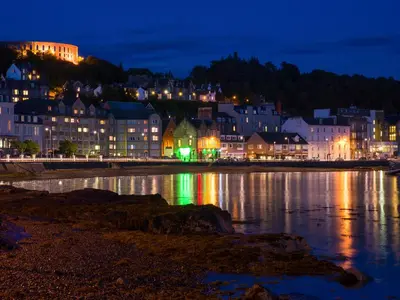 a city at night with lights on the water at Littlebay Apartment in Oban
