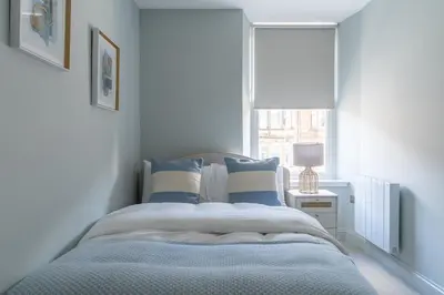 a bed with blue and white pillows and a window at Prime Stay Apartments in Paisley