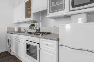 a white kitchen with white cabinets and a refrigerator at Free Parking - City Centre - Stunning Views - Great Location in Edinburgh