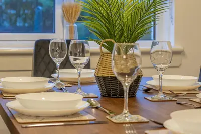 a wooden table with wine glasses and plates on it at Boswell House - Modern 3 Bed House East Kilbride Close to Motorway in East Kilbride