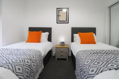 two beds with orange pillows in a room at Sonas Apartment in Greenock