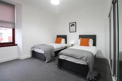two beds in a room with white walls and orange pillows at Sonas Apartment in Greenock