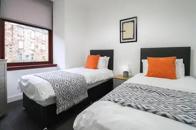 two beds with orange pillows in a room at Sonas Apartment in Greenock