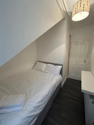 a bedroom with a bed with white sheets and a light at The Bay View Apartment in Gourock