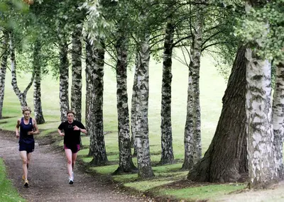 a man and woman running down a trail in the woods at Willow Court in Stirling