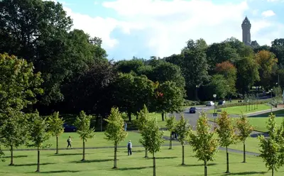 people walking in a park with trees and a clock tower at Willow Court in Stirling