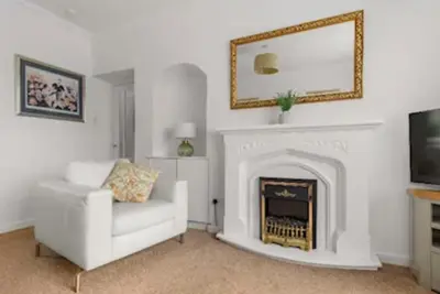 a living room with a white chair and a fireplace at Grangeburn Residence - 2 bedroom home with parking in Falkirk