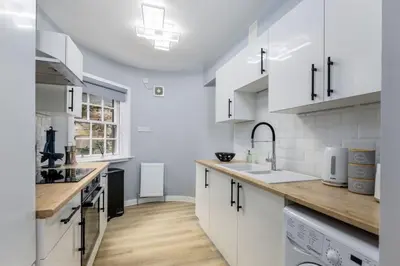 a kitchen with white cabinets and a wooden counter top at Castle Esplanade Apartment in Stirling