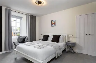 a white bedroom with a large bed and a chair at Castle Esplanade Apartment in Stirling