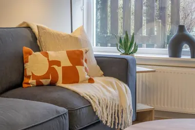 a grey couch with an orange and white throw pillow at Hawick Apartment- 2-Bed in Coatbridge, Mins from Motorway to Glasgow in Old Monkland