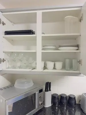 a kitchen with white cabinets and plates and a microwave at Modern & Cosy 3 Bedroom Inverkeithing home- Ideal for Edinburgh Dunfermline & St Andrews with Free Parking in Inverkeithing