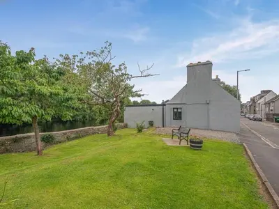 a building with a bench in the grass near a street at Creebank Cottage with river view in Newton Stewart