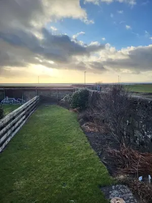 a backyard with a retaining wall and a grass field at The Wee House -Coorie Doon Stays in Troon