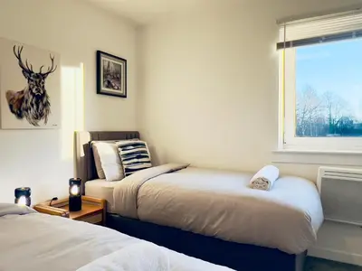 a bedroom with two beds and a window with a deer head on the wall at Chic & Cozy 2-Bed Flat in Glasgow - Free Parking in Glasgow