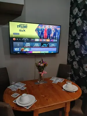 a wooden table with a television on a wall at Sunset of Largs in Largs