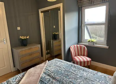 a bedroom with a bed and a chair and a mirror at Coorie Neuk in Cairnbaan