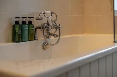 a bath tub with a shower head and bottles on a shelf at Scenic Oaklodge with wood burner in Saint Fillans