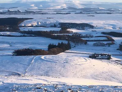 a snow covered hill with trees and mountains in the distance at Garden Retreat in Nine Mile Burn