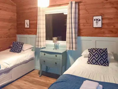 a bedroom with two beds and a table with a lamp at Grouse Lodge in Dunoon