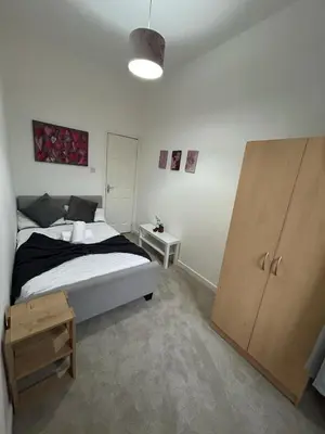 a bedroom with a bed and a wooden cabinet at Cozy, modern flat in Govan in Glasgow