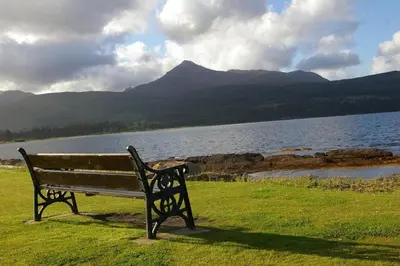 a bench sitting on the grass near a body of water at The Shorehouse in Brodick
