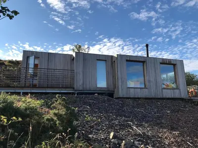 a modular house with windows on top of a field at Cala Fearnadh Off-Grid cabin, Bunessan, Mull in Bunessan