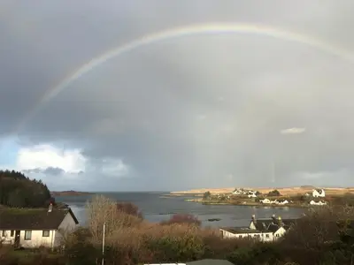a rainbow in the sky over a body of water at Cala Fearnadh Off-Grid cabin, Bunessan, Mull in Bunessan