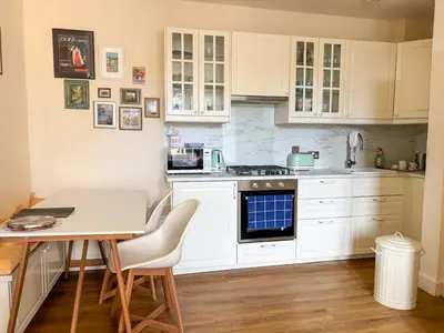 a kitchen with white cabinets and a table at Bright Top Floor 2BR Apartment in Morningside, Easy City Centre Links, Close to University and Royal Hospital in Edinburgh
