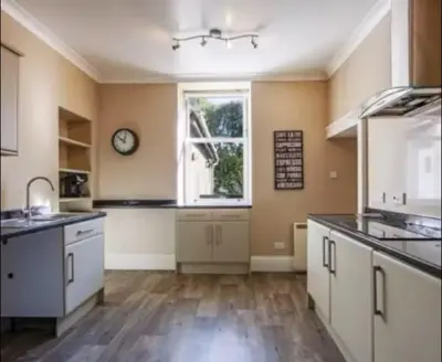 a kitchen with white cabinets and a clock on the wall at Snug Loft Room, Room 5, Beautiful Connel near Oban in Connel