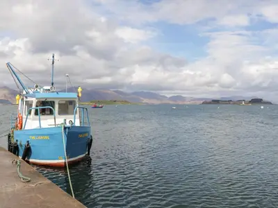 a blue boat in the water next to a dock at Tirlaggan Studio in Oban