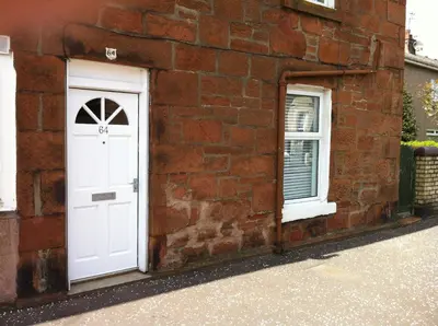 a brick building with a white door and two windows at Apartment Caerlaverock Road in Prestwick