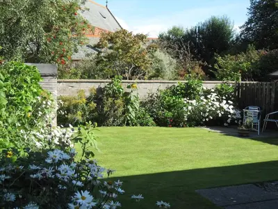 a garden with a lawn with flowers and a fence at Church Cottage with sunny garden in Ayr