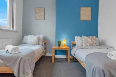 two beds in a room with blue walls and a table at Vacant Nests The Grampian Free Wifi in Wishaw