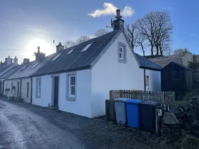 a white house with trash cans in front of it at Campbell Cottage in Biggar